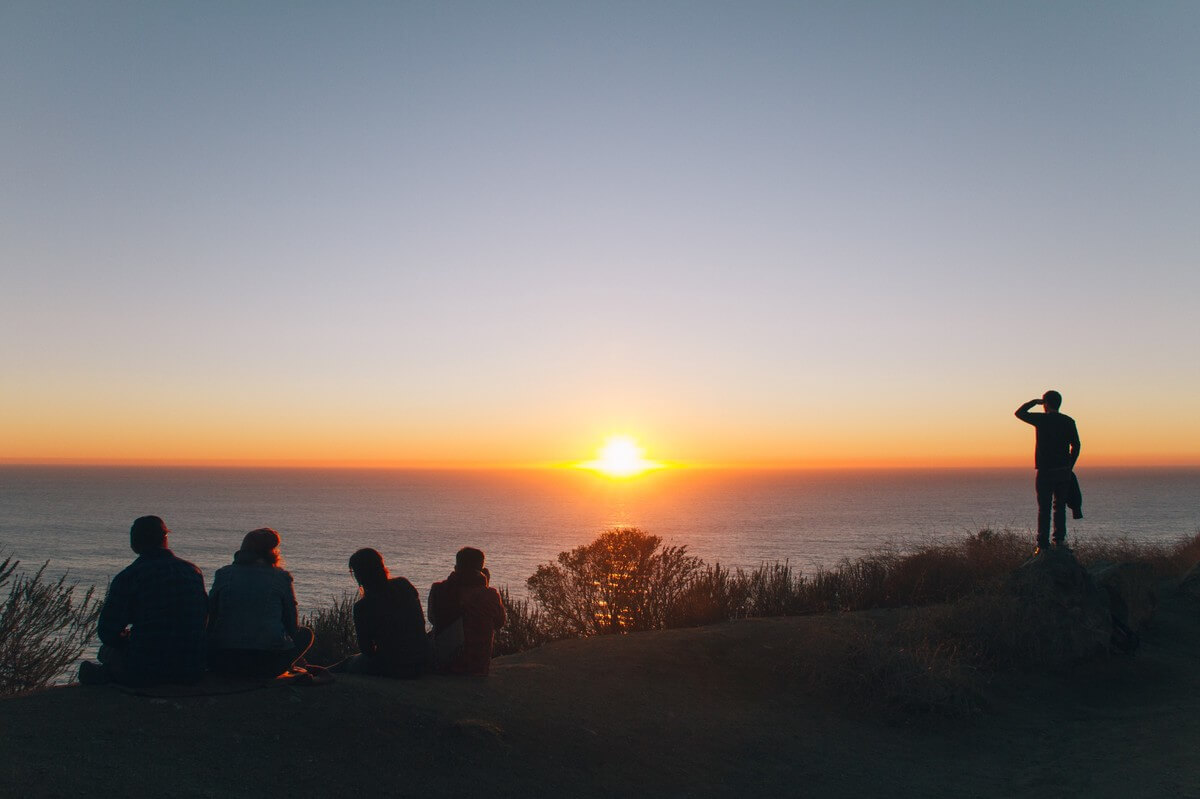 peoples on hill near ocean at golden hour
